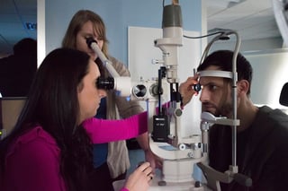 Regional Sales Representative, Lena Zhuk, receives assistance from Dr. Stephanie Leburg adjusts her slit lamp to get a perfect retinal view on PCO student Kyle Keyser .